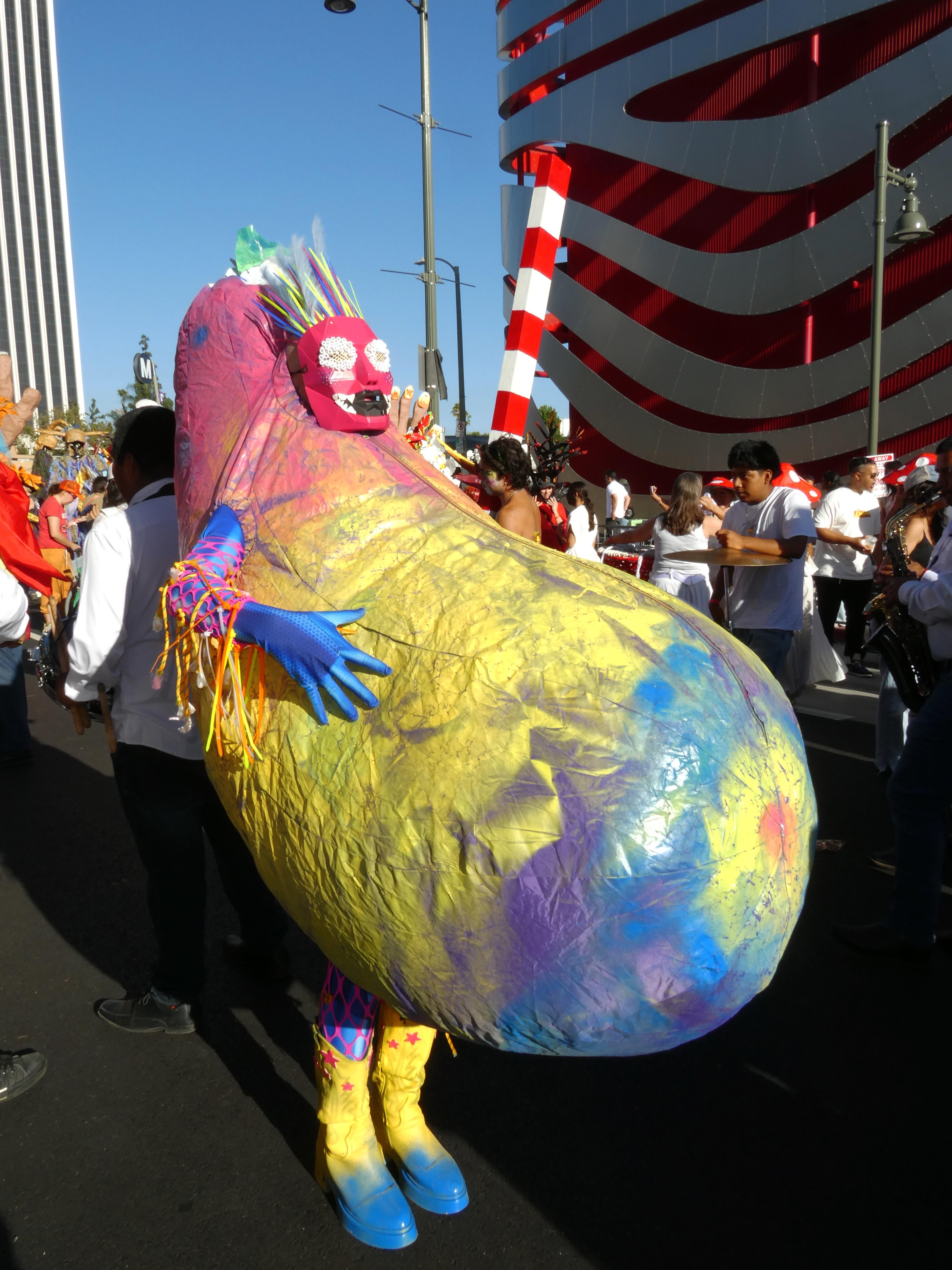 Jesse posing in a Colorful eggplant shaped inflatbale outfit in a crowded parade setting.